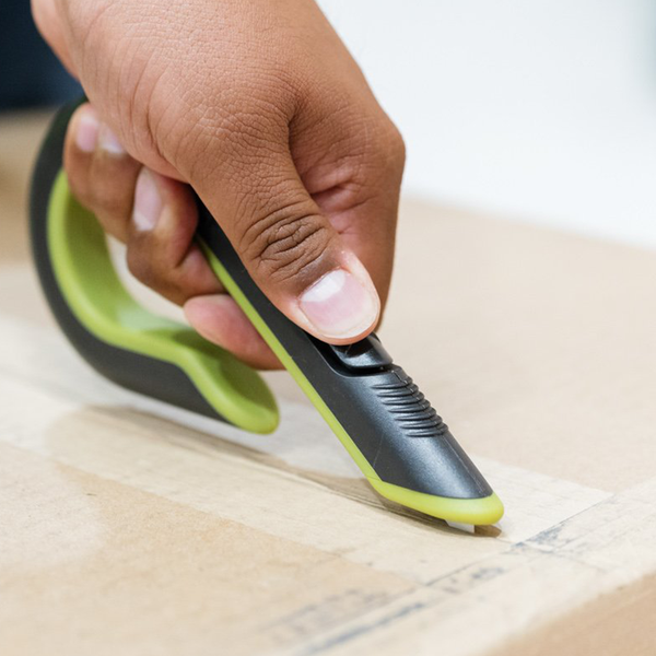 Hand benutzt ein ergonomisches Sicherheitsmesser zum Öffnen eines Kartons.
