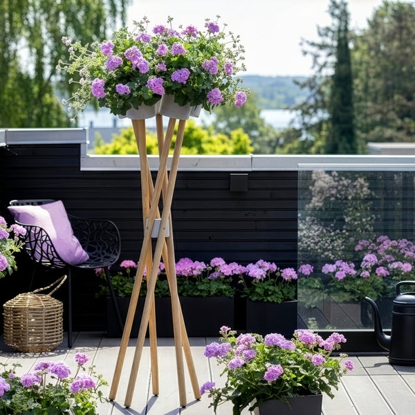 Hoher Pflanzenständer aus Holz mit lila Blumen auf einem modernen Balkon mit dunkler Verkleidung und Gartenmöbeln.