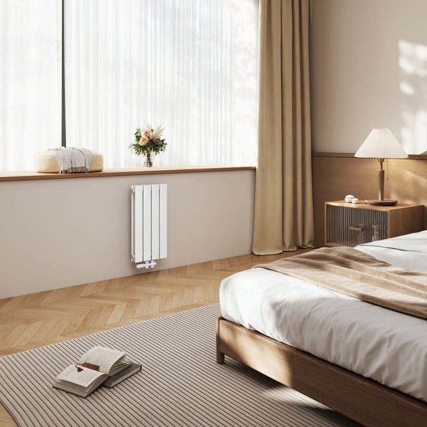 Moderner Designheizkörper montiert in einem gemütlichen Schlafzimmer mit Holzbett, Fischgrätparkett und lichtdurchfluteten Vorhängen.