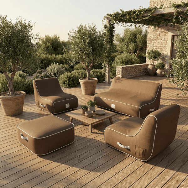 Modernes Garten-Lounge-Set aus Stoff mit Sofa, Sesseln, Hocker und Holztisch auf einer hellen Holzterrasse mit Olivenbäumen.