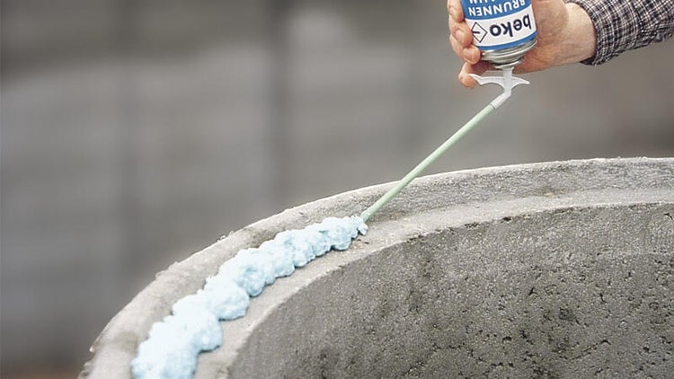 Anwendung von Beko Brunnenschaum auf einem Betonring mit einem Sprührohr.