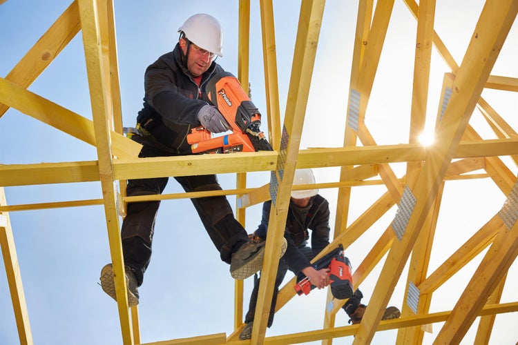 Zwei Handwerker befestigen mit einem Druckluftnagler Holzbalken auf einer Baustelle.