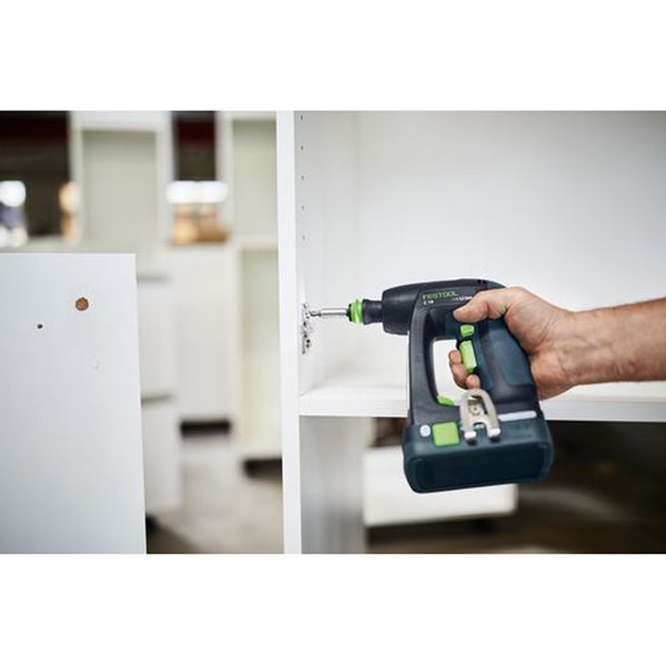 Eine Hand hält einen Akku Bohrschrauber von Festool und schraubt ein Scharnier an ein weißes Möbelbauteil.