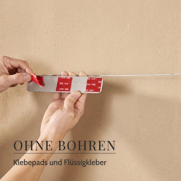 Hände halten eine Metallleiste mit Klebepads an einer Wand zur Montage ohne Bohren.