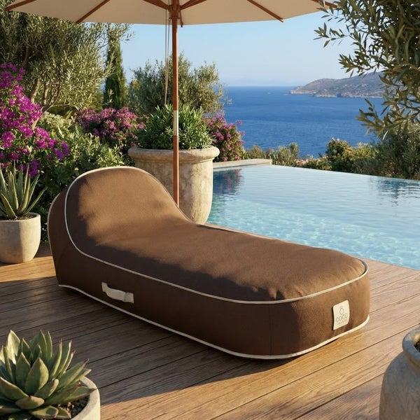 Braune Outdoor-Liege in Sitzsack-Form auf einer Holzterrasse am Pool mit Meerblick und COCO Logo, modernes Design, helle und weitläufige Umgebung.