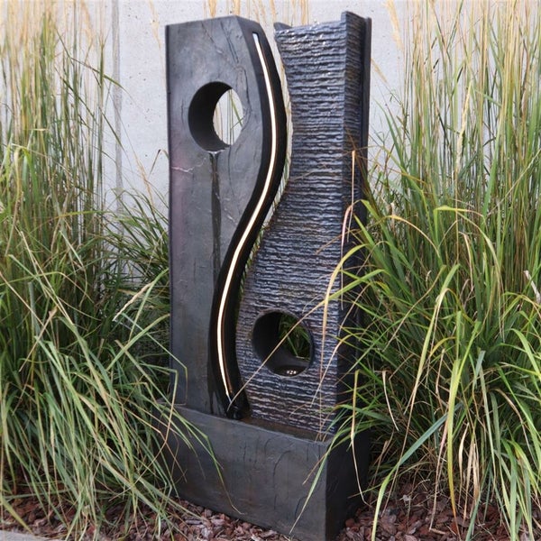 Gartenbrunnen mit zwei Wasserelementen und LED-Beleuchtung inmitten von Ziergräsern