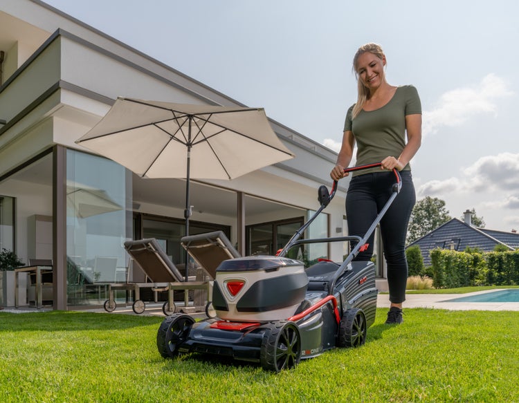Eine Frau mäht den Rasen vor einem modernen Haus mit einer Al-Ko 2 in 1 Rasenmäher Einheit an einem sonnigen Tag.