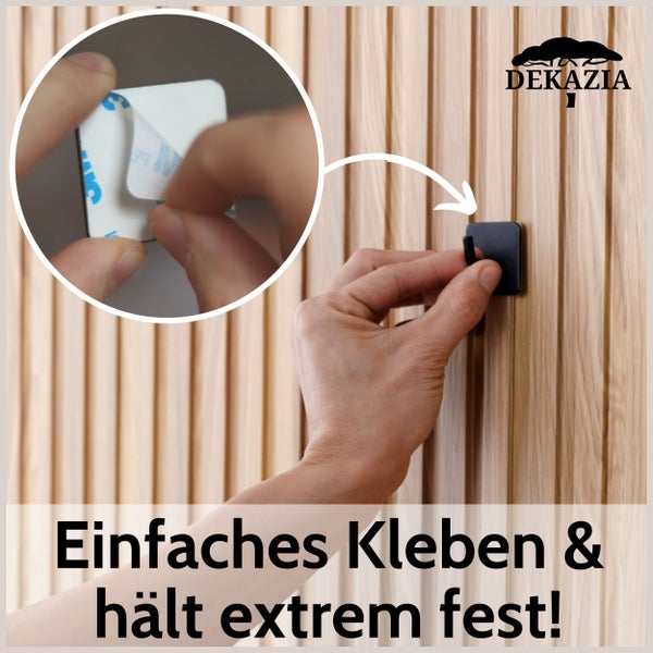 Eine Person bringt einen selbstklebenden Wandhaken von Dekazia auf einer Holzlamellenwand an. Detailansicht zeigt das Abziehen der Schutzfolie.