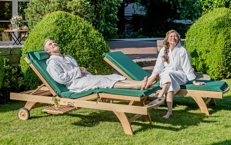 Zwei Personen entspannen auf Gartenliegen mit grünen Auflagen im Freien.