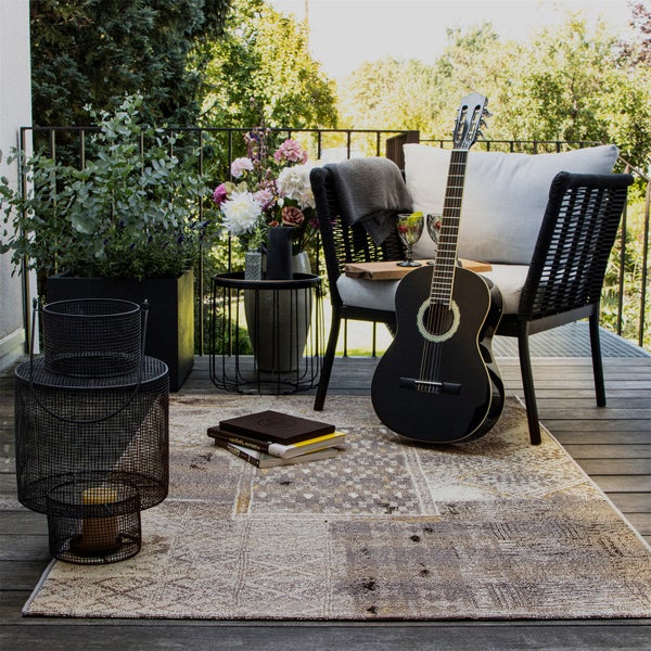 Gemütlich gestalteter Balkon mit geflochtenem Sessel, Outdoorteppich, Akustikgitarre, Windlicht und Pflanzen auf einer Holzterrasse.