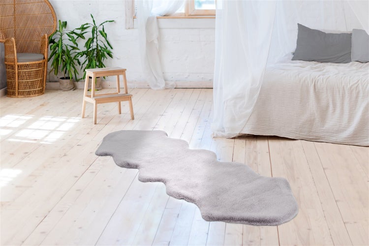 Langer, flauschiger Kunstfell-Teppich auf hellem Holzboden in einem hellen Schlafzimmer mit Bett und Pflanzen.