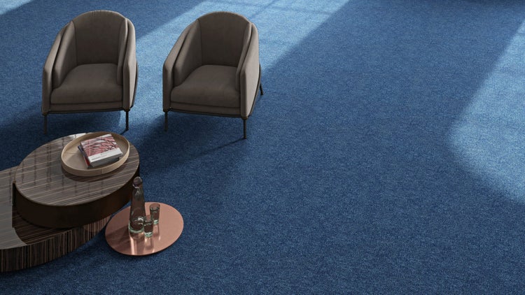 Moderner, heller Raum mit blauem Teppichboden, zwei grauen Sesseln und einem mehrstufigen Couchtisch aus Holz.