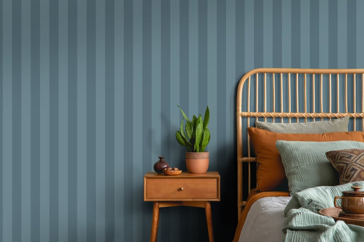 Schlafzimmer mit Bett, Nachttisch und Zimmerpflanze vor einer blau gestreiften Wand