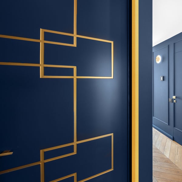 Detailaufnahme einer blauen Tür mit goldenen geometrischen Verzierungen und einem angrenzenden Raum.