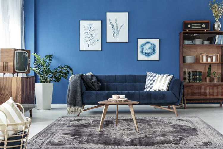 Helles Wohnzimmer im Mid-Century-Stil mit Samtsofa, Holz-Couchtisch und gemustertem Teppich. Holzregal, Retro-Fernseher und Zimmerpflanze.