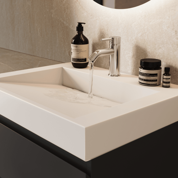 Modernes Badezimmer mit weißem Mineralguss-Waschbecken auf dunklem Unterschrank, verchromte Armatur mit Wasserstrahl und Badaccessoires.