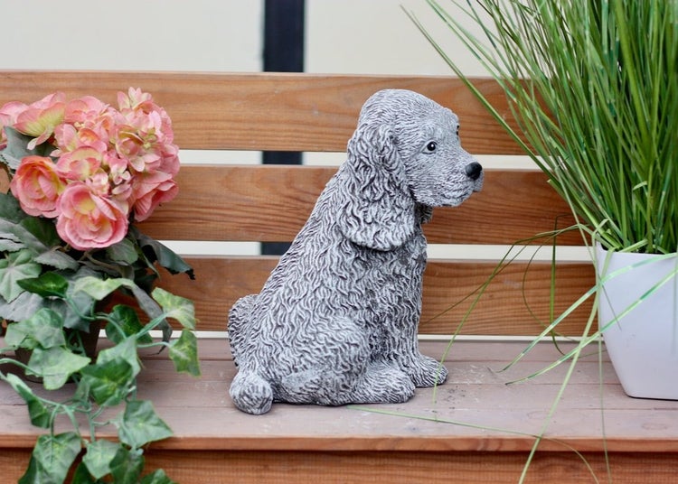 Gartenfigur sitzender Hund in Steinoptik auf einer Holzbank neben Pflanzen