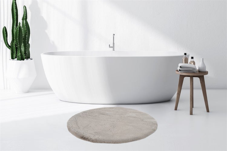 Runder, flauschiger Badteppich in Beige vor einer freistehenden Badewanne in einem hellen, modernen Badezimmer.