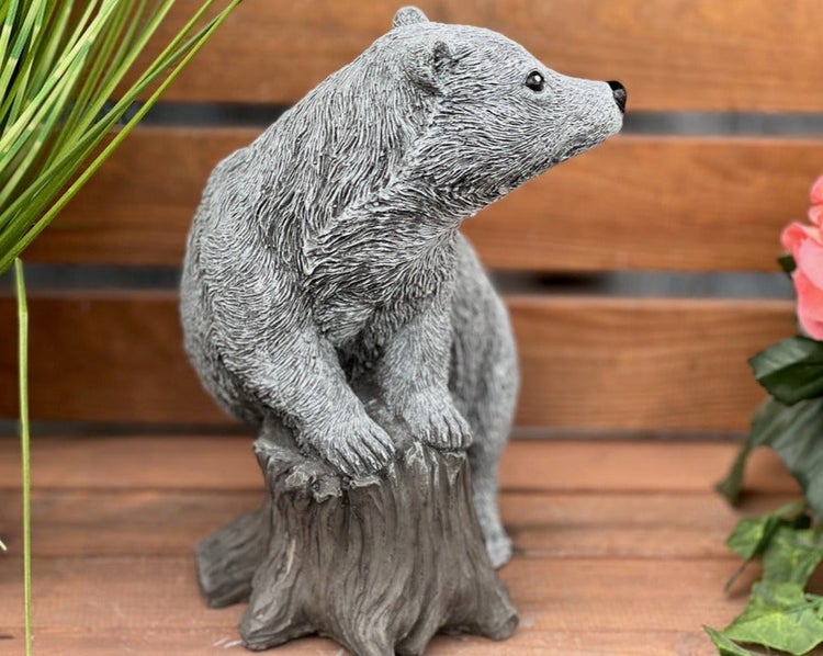 Detaillierte Gartenfigur aus Stein in Form eines jungen Bären, der auf einem Baumstumpf sitzt.