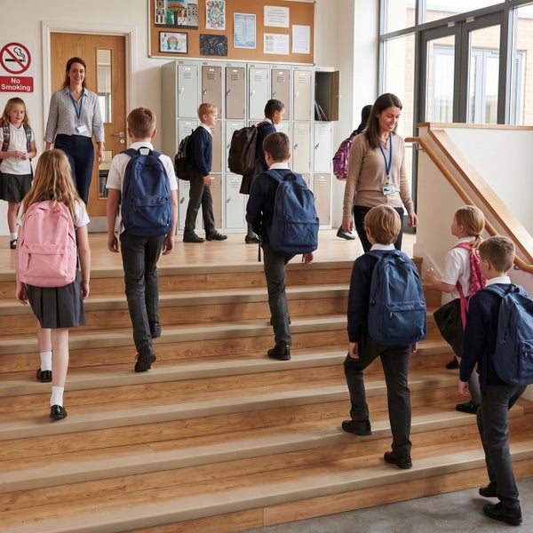 Schüler in Schuluniform gehen eine Holztreppe in einer Schule hinauf während Lehrerinnen sie begleiten, im Hintergrund Schließfächer.