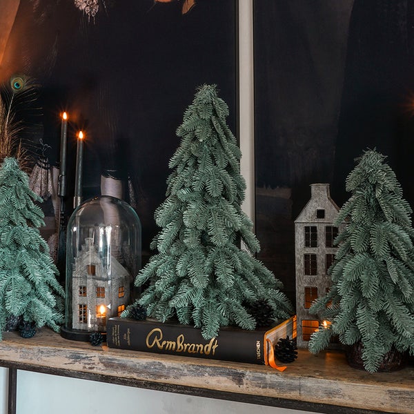 Dekorative Weihnachtsszene mit Kunstbäumen, einem Buch mit dem Titel Rembrandt und einem Haus aus Metall