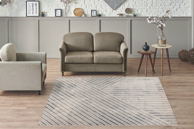 Rechteckiger Teppich mit geometrischem Linienmuster in einem modern eingerichteten Wohnzimmer mit Sofa, Sessel und Holzboden.