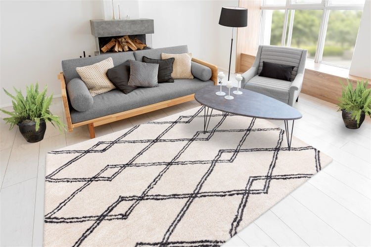 Rechteckiger Teppich mit geometrischem Muster in einem hellen Wohnzimmer mit Sofa, Sessel, Couchtisch und Zimmerpflanzen.