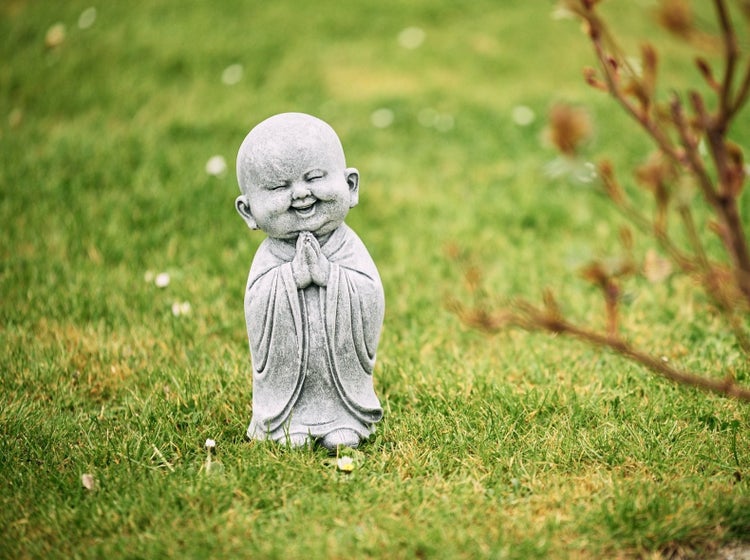 Steinfigur kleiner lachender Buddha in Gebetshaltung als Gartendeko.