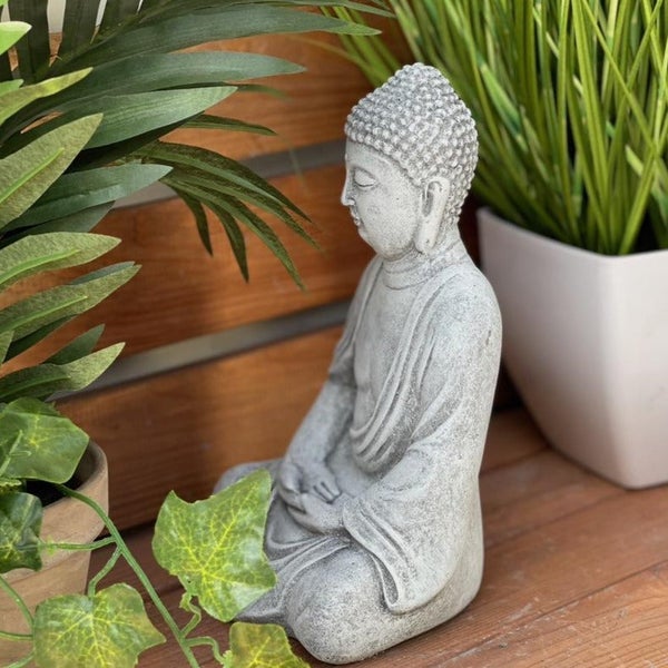 Sitzende Buddha Figur aus Stein für den Garten als dekoratives Element zwischen grünen Pflanzen