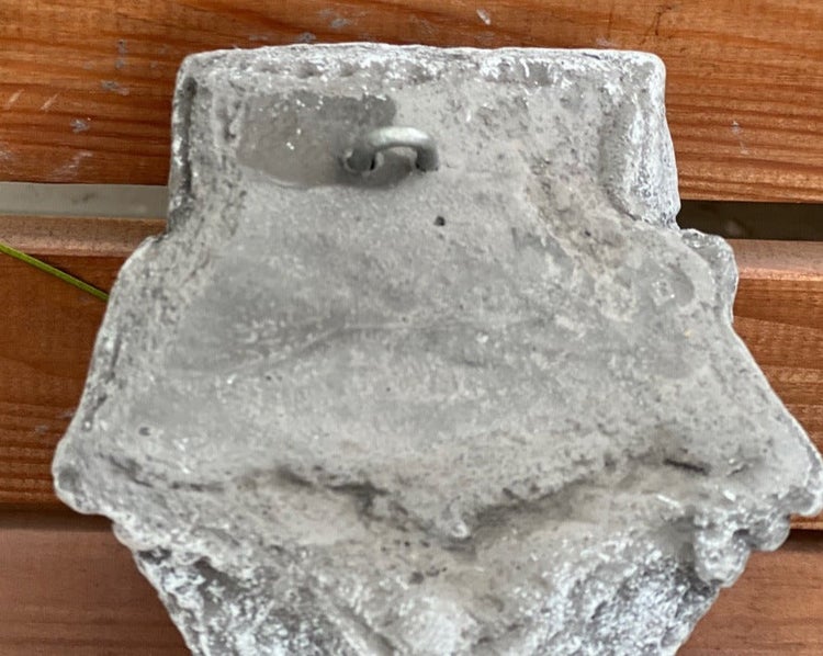 Rückseite einer Wanddekoration aus Beton mit integrierter Metallschlaufe zum Aufhängen.
