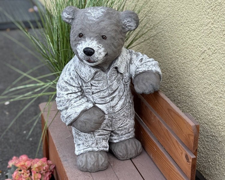 Gartenfigur Teddybär mit Latzhose aus Kunststein, stehend neben einer kleinen Holzbank