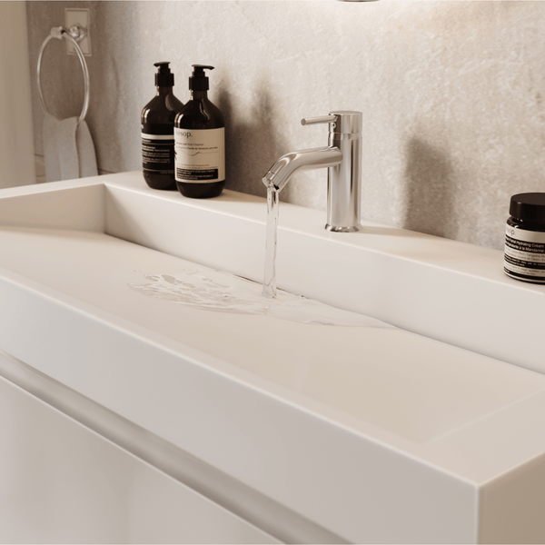 Modernes Badezimmer mit einem minimalistischen Waschbecken und einer verchromten Armatur. Wasser fließt aus dem Hahn. Seifenspender im Hintergrund.
