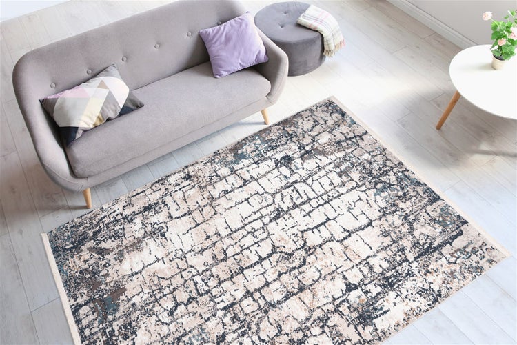 Modernes Wohnzimmer mit rechteckigem Teppich mit abstraktem Gittermuster auf hellem Boden neben einem grauen Sofa und Beistelltisch.