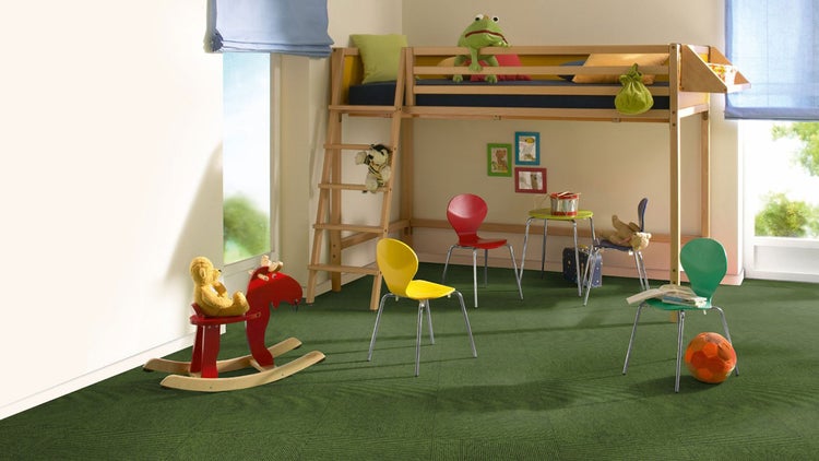 Helles Kinderzimmer mit grünen Teppichfliesen, einem Hochbett aus Holz, bunten Stühlen und einem roten Schaukelpferd.