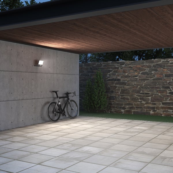 LED Außenwandleuchte montiert an einer Betonwand unter einem modernen Carport mit Fahrrad und Steinmauer im Hintergrund