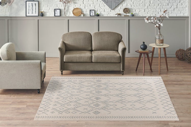 Rechteckiger Teppich mit geometrischem Ethno-Muster in einem hellen Wohnzimmer mit Sofa, Sessel und Parkettboden.