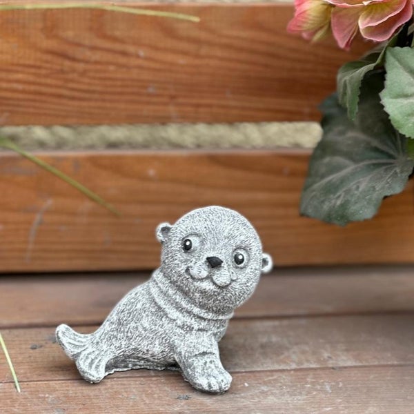 Gartenfigur Seehund in Steinoptik, dekorative Tierfigur für den Außenbereich auf Holzterrasse platziert.