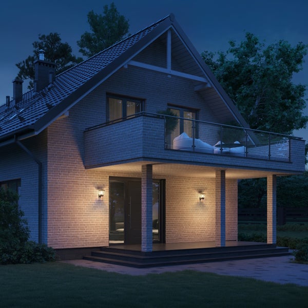 Einfamilienhaus mit Ziegelmauerwerk und Balkon bei Nacht, beleuchtet durch Außenwandleuchten an der Terrasse.