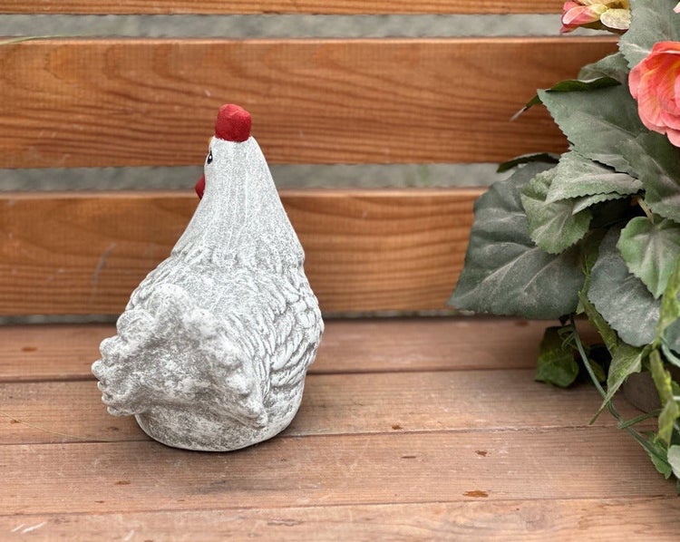 Dekorative Gartenfigur in Form eines Huhns aus Steinoptik auf einer Holzbank.