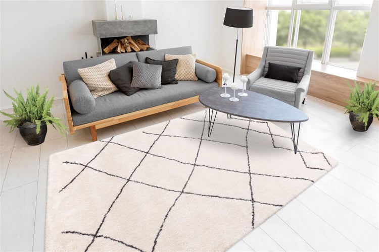 Helles modernes Wohnzimmer mit einem cremefarbenen Teppich mit schwarzem Rautenmuster, grauem Sofa und Couchtisch.