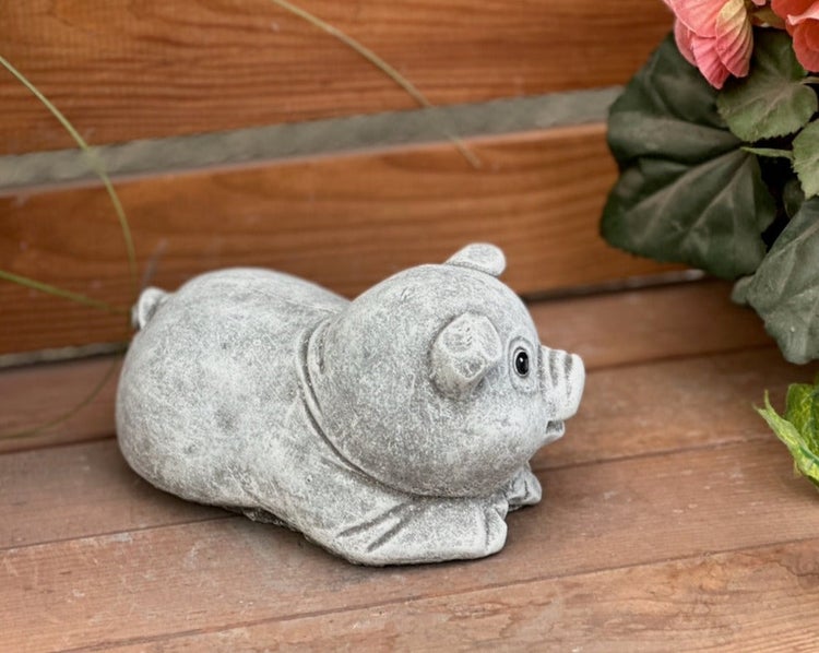 Dekorative Gartenfigur in Form eines liegenden Schweins aus grauem Kunststein.