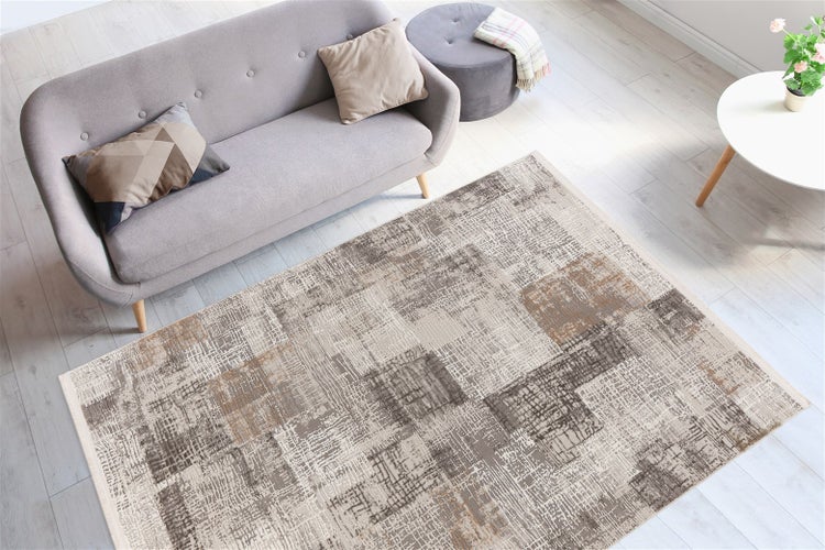 Moderner rechteckiger Teppich mit abstraktem Karomuster in Grau und Beige in einem hellen Wohnzimmer vor einem grauen Sofa auf hellem Holzboden.