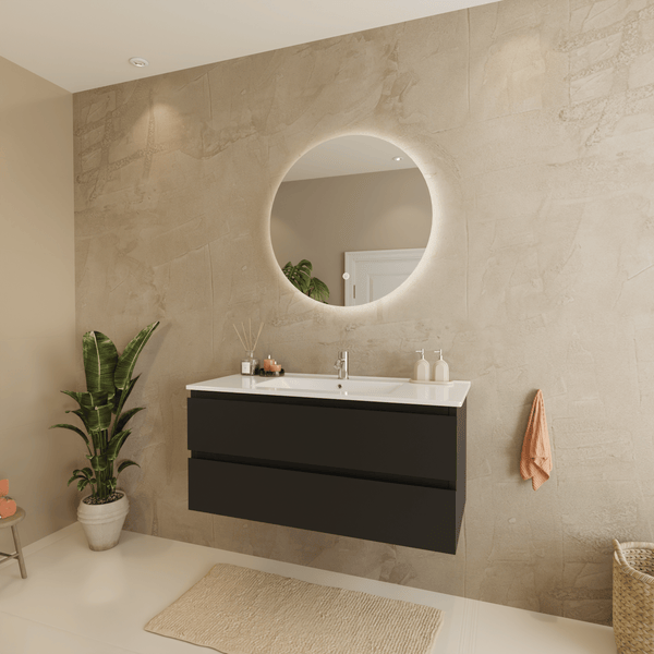 Modernes Badezimmer mit dunkelgrauem Waschtisch, weißem Waschbecken, rundem beleuchtetem Spiegel und strukturierten beige Wänden.