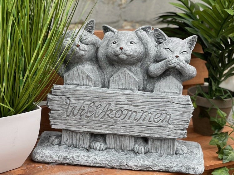 Gartendekoration aus Stein mit drei Katzen, die sich Augen, Ohren und Mund zuhalten und ein Schild mit der Aufschrift Willkommen tragen.