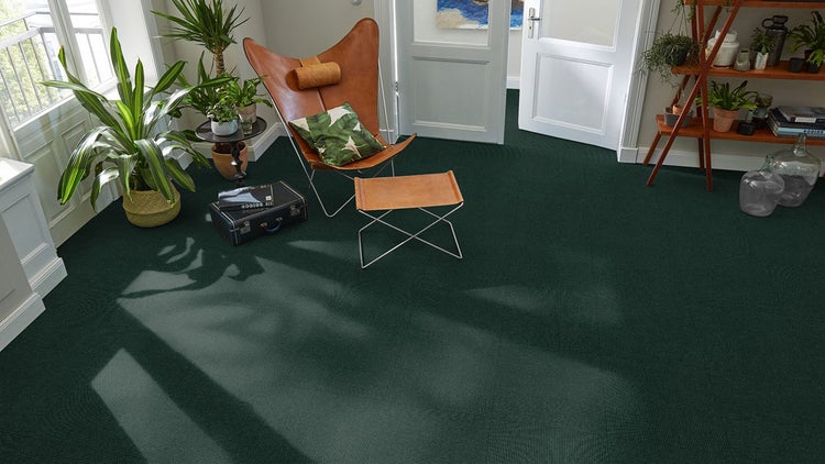 Dunkelgrüne Teppichfliesen mit Rippenstruktur in einem hellen Wohnzimmer mit Ledersessel und Zimmerpflanzen.