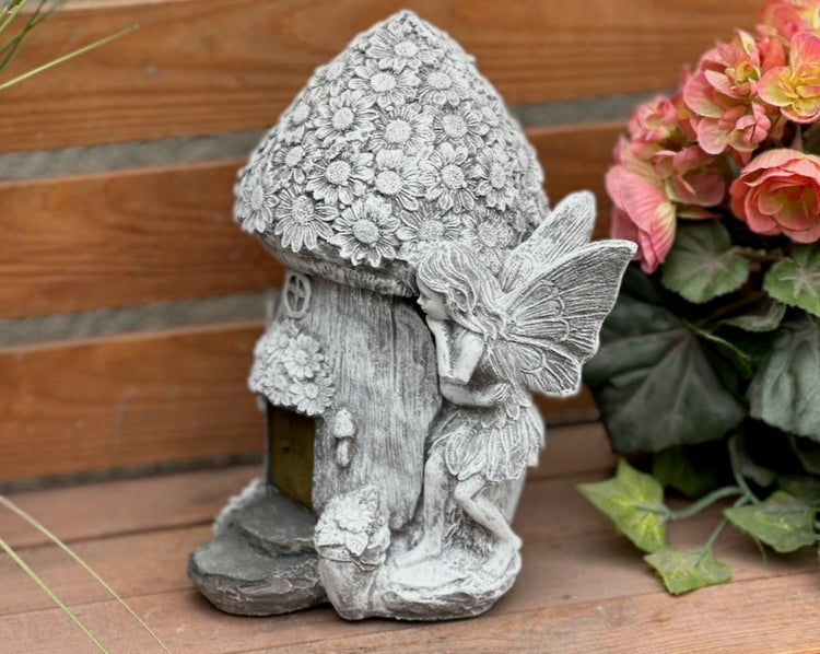 Gartenfigur einer Fee an einem Pilzhaus aus Steinguss für die dekorative Gartengestaltung.