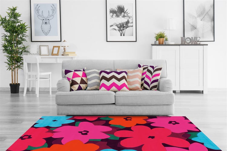 Farbenfroher Blumenteppich in einem hellen Wohnzimmer mit grauem Sofa, gemusterten Kissen und weißer Einrichtung.