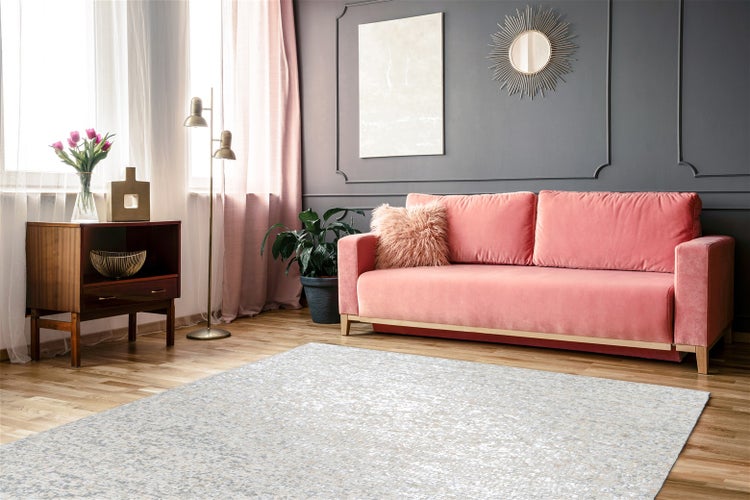 Heller, gemusterter Teppich in einem hellen Wohnzimmer mit rosa Sofa, Holzkommode und grauer Wand mit Sonnenspiegel.