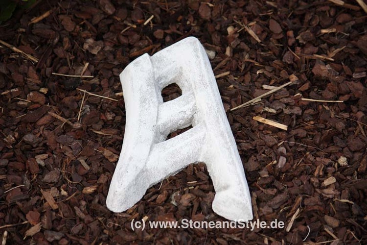 Steinbuchstabe A als Gartendekoration aus witterungsbeständigem Material liegend auf Rindenmulch.