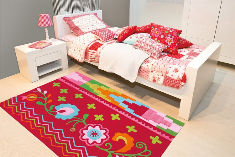 Helles Kinderzimmer mit weißem Einzelbett, buntem Teppich mit Blumenmuster und weißem Nachtschrank.